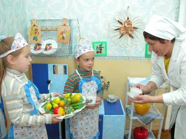 Дети в фартуках держат тарелку с муляжами фруктов