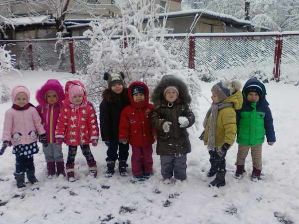 Дети на зимней прогулке стоят около забора
