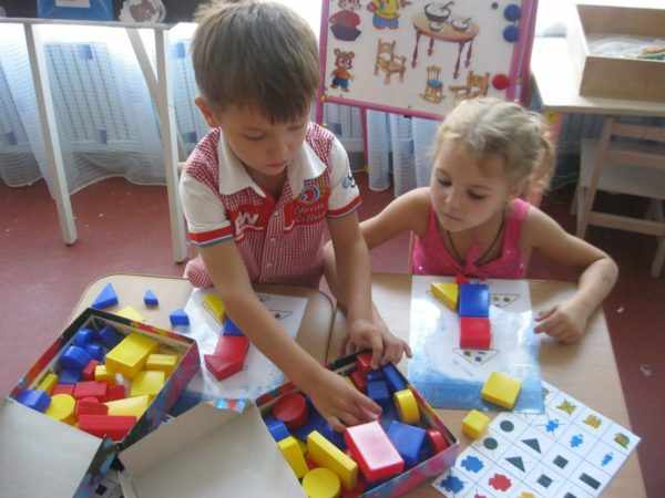 Мальчик и девочка составляют изображениеиз блоков по схеме