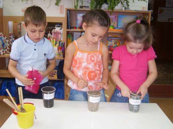 Трое детей изучают свойства песка, земли и глины