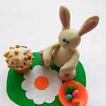 Кролик на цветочной лужайке рядом с куличиком и тарелкой с яичками