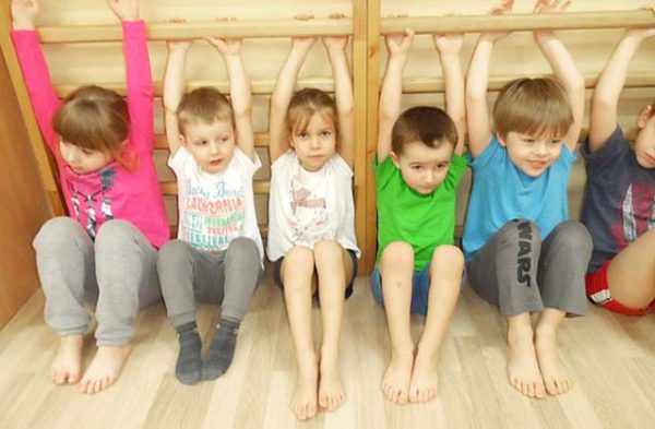 Дети держатся за нижние рейки гимнастической стенки