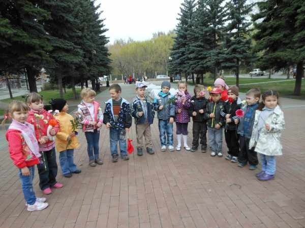 Дети с гвоздичками стоят полукругом на улице