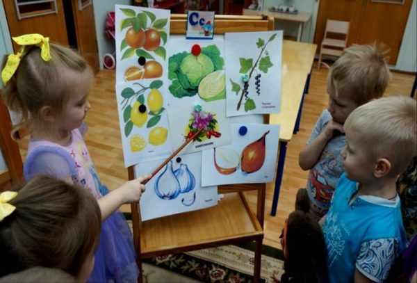 Девочка показывает указкой на картинки с фруктами и овощами
