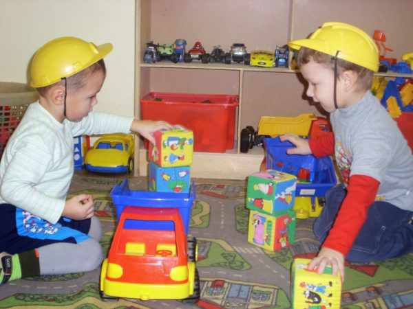 Два мальчика в строительных касках играют с кубиками и машинками