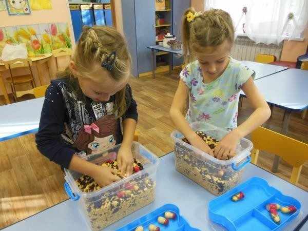 Две девочки выбирают игрушки из контейнеров с крупами