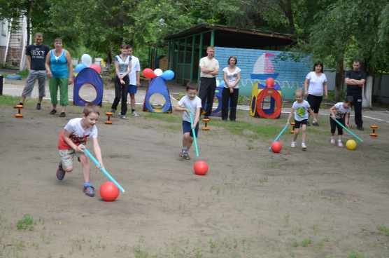 Дети на площадке участвуют в летнем спортивном мероприятии, родители наблюдают
