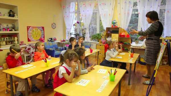 Педагог обращается к дошкольникам, сидящим за партами