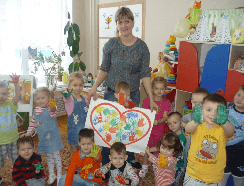Воспитатель и дети держат картину из сердечек ладошками