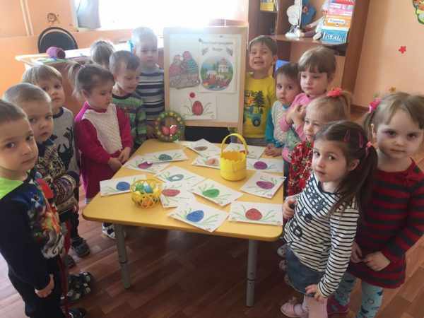 Дети стоят вокруг стола с рисунками крашеных яиц