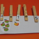 Прищепки с цифрами и математическими знаками на листе с изображением яблок