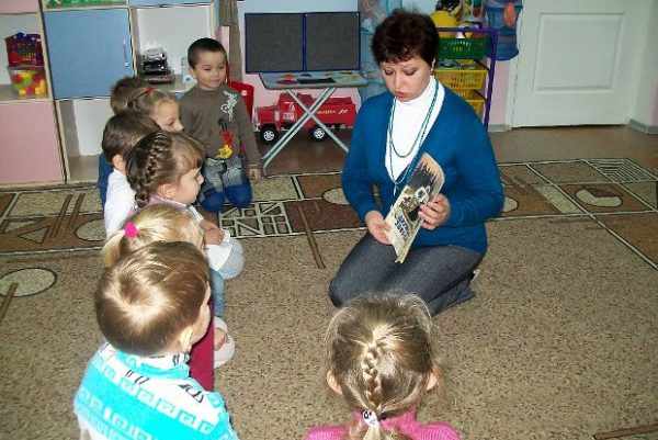 Воспитатель показывает детям, сидящим полукругом, картинку на книжке