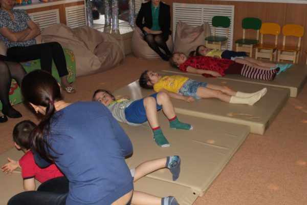 Педагог помогает детям выполнять упражнения лёжа