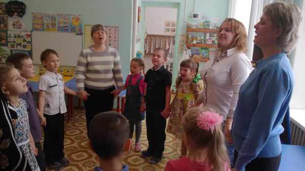 Дети, воспитательница и две мамы, взявшись за руки в хороводе, поют