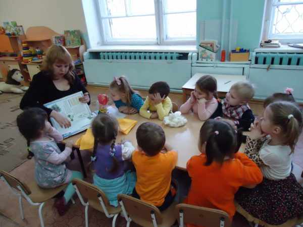 Воспитательница показывает картинку в книге, дети сидят за столом