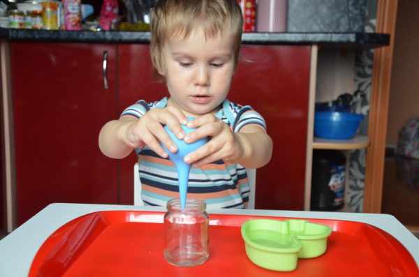 Мальчик переливает воду из формочки в стеклянную баночку с помощью спринцовки