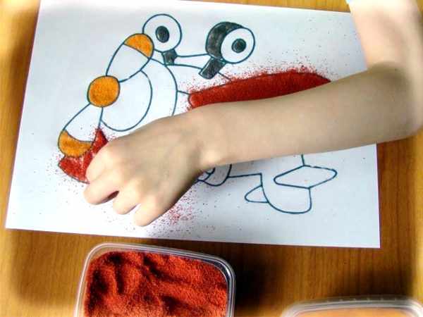 Ребёнок раскрашивает рисунок цветным песком