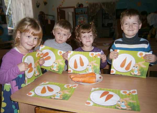 Четверо детей сидят за столом, держа в руках изображения морковок