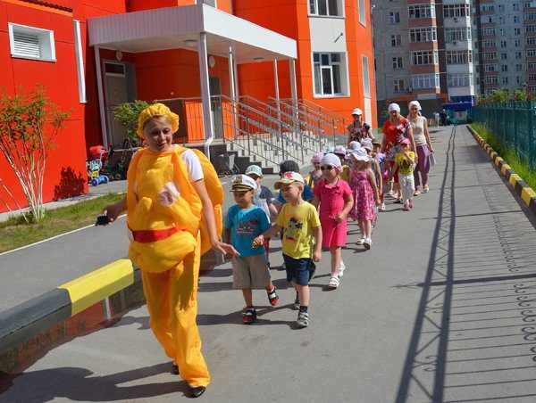 Воспитательница в жёлтом карнавальном костюме ведёт строй детей