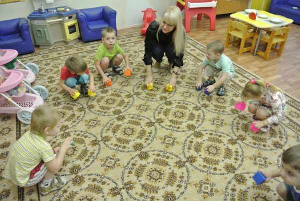 Дети с воспитательницей в кругу на ковре передвигают по полу кубики