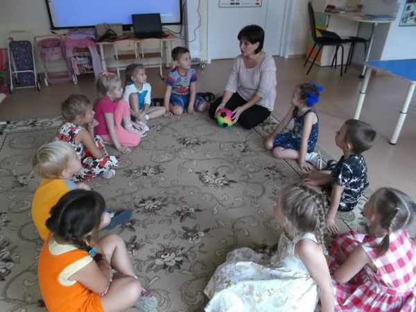 Дети и воспитательница с мячом в руках сидят в кругу на ковре