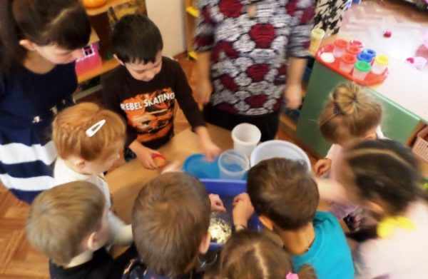Дети стоят вокруг стола с пластиковыми стаканчиками с семенами