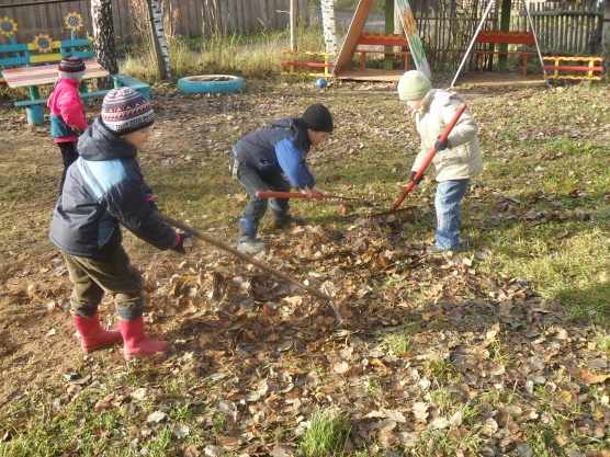 Дети граблями сгребают листья на садовом участке