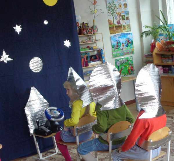 Трое детей, сидя на стульях, играют в космическое путешествие