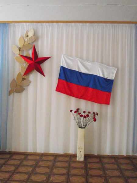 Стена украшена флагом России, звездой и вазой с букетом гвоздик