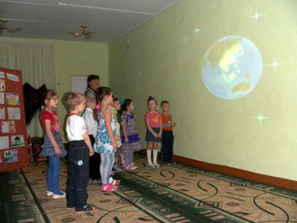 Дети и воспитатель смотрят на изображение Земли на стене