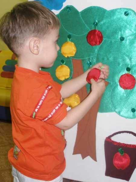 Мальчик вешает на дерево игрушечное яблоко