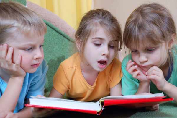 Две девочки и мальчик читают книгу