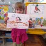 Девочка держит рисунок снегиря ватными палочками
