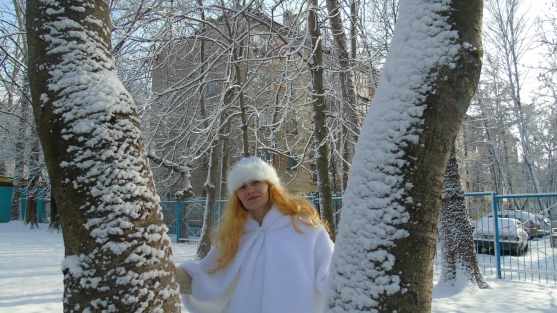 Девушка в костюме Зимушки-зимы стоит между деревьев