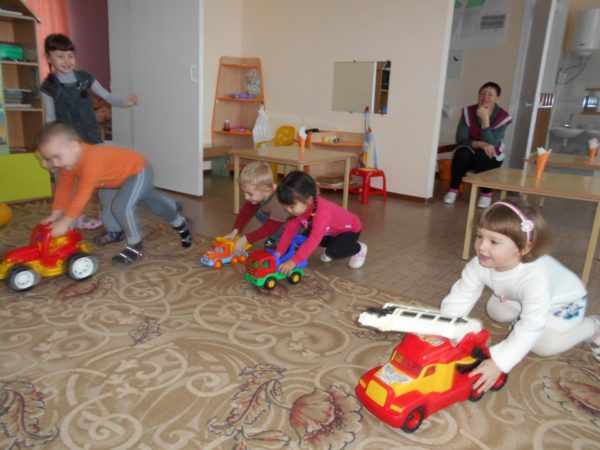 Дети катают большие машинки по ковру