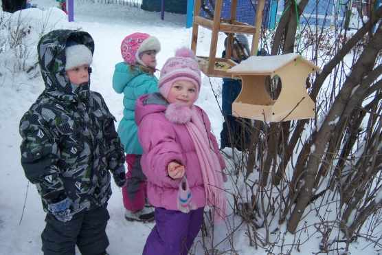 Дети в зимней одежде стоят около птичьих кормушек