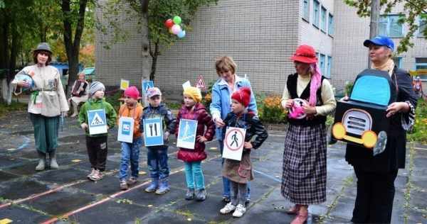 Дети стоят с изображениями дорожных знаков, воспитатели в костюмах