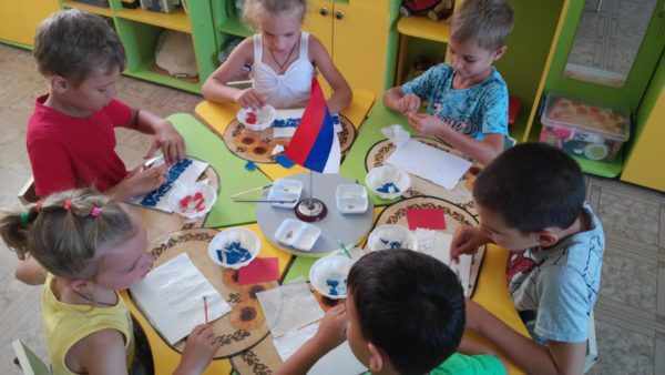 Дети сидят за столом и выполняют аппликацию Флаг России