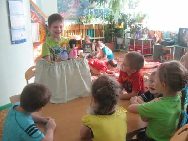 Мальчик показывает представление с куклами, дети сидят за столом и смотрят