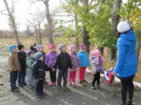 Воспитательница показывает детям листья на осенних деревьях