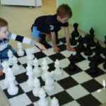 Два мальчика играют в напольные шахматы большого размера