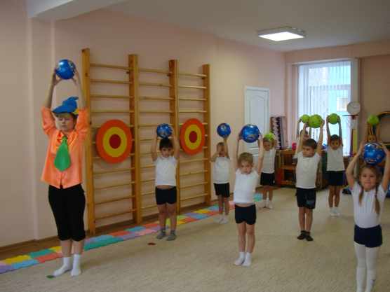 Дети и педагог в костюме Незнайки стоят с поднятыми вверх мячами