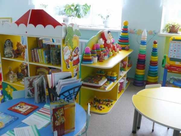 Детская мебель с игрушками, книгами на полках, справа стол из двух полуокружностей
