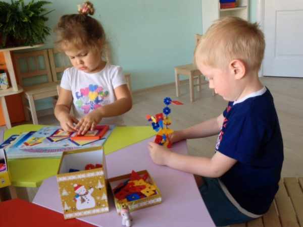 Девочка и мальчик играют игрушками для развития мелкой моторики: палочками и фигурками пирамиды
