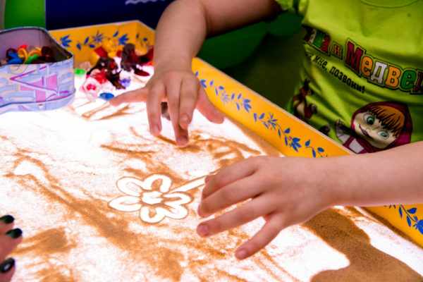 Ребёнок рисует песком на специальной доске