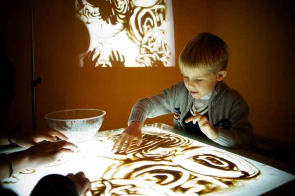 Мальчик рисует песком на специальном столе с подсветкой