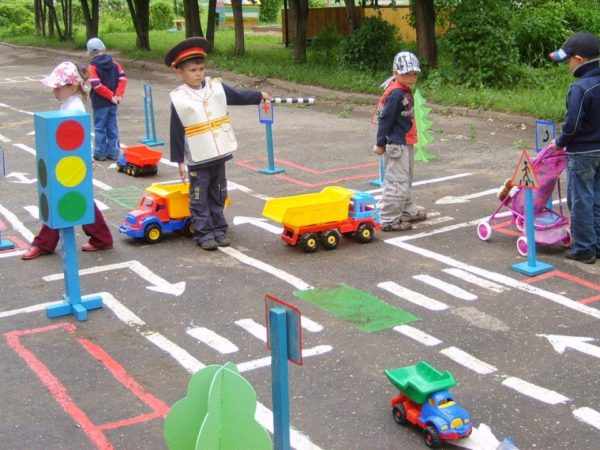 Дети играют с машинками на площадке с дорожными знаками и светофорами