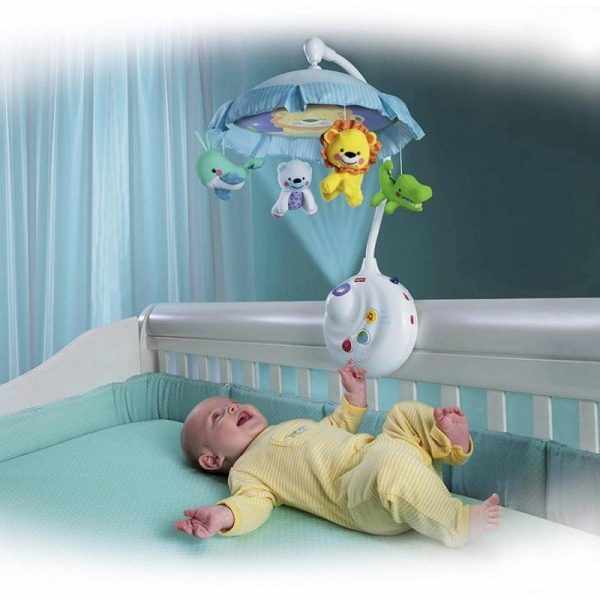 Младенец в кроватке смотрит на мобиль, трогает его и смеётся