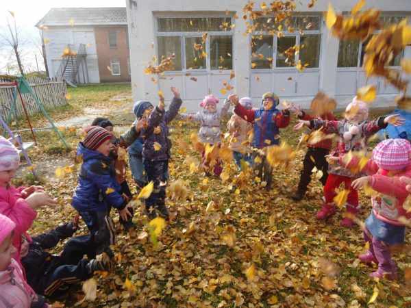 Дети подбрасывают вверх осенние листья на прогулке