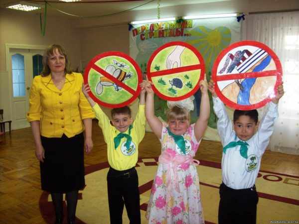 Воспитательница и трое детей, держащих знаки о поведении на природе
